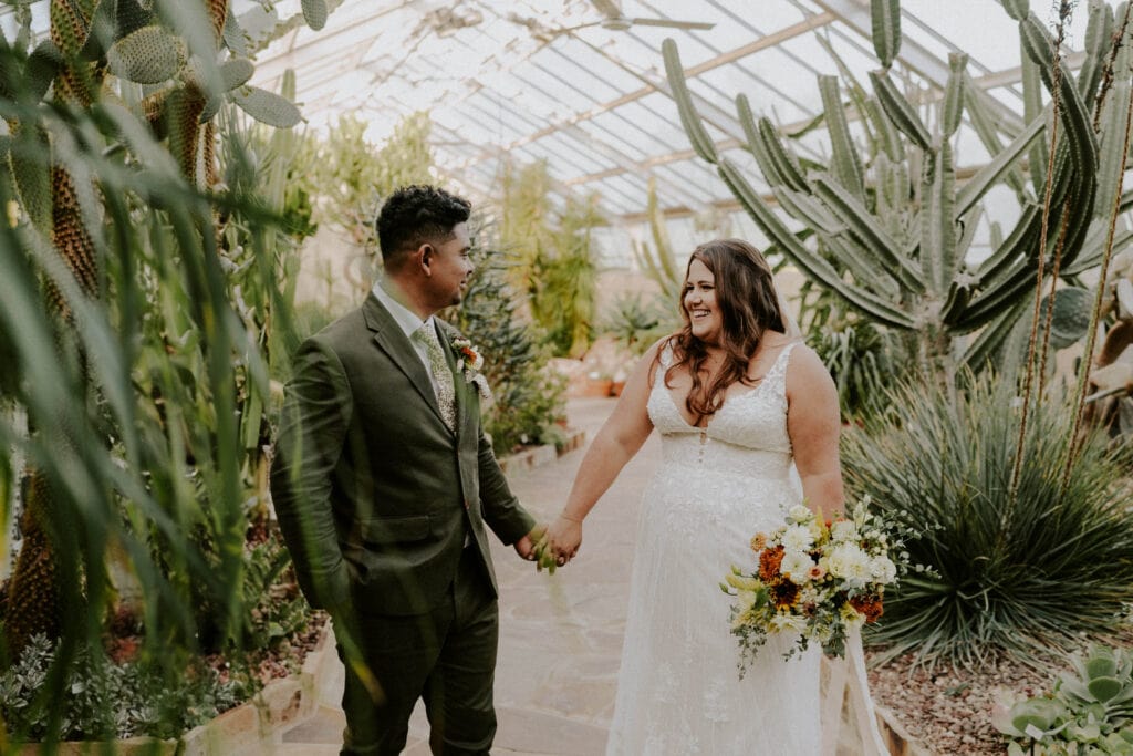 bride and groom walking holding hands by tropical plants in indoor gardens