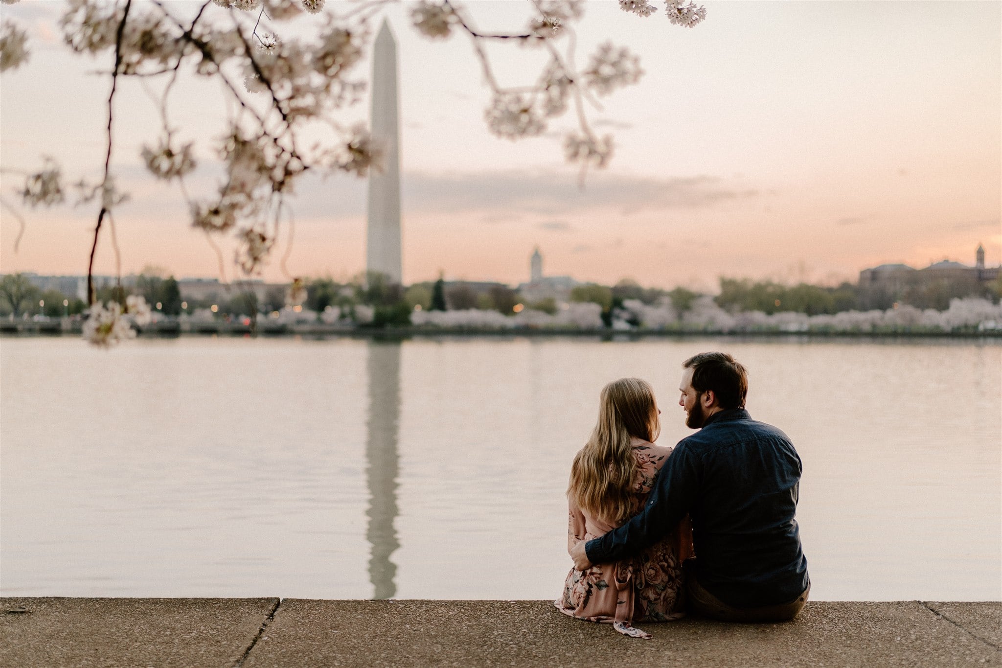 Couple sitting at tidal basin watching sunrise with cherry blossoms