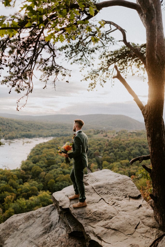 Groom standing on edge of mountain with bouquet
