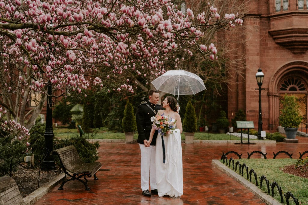 Bride and groom standing in the rain with umbrella and magnolia trees