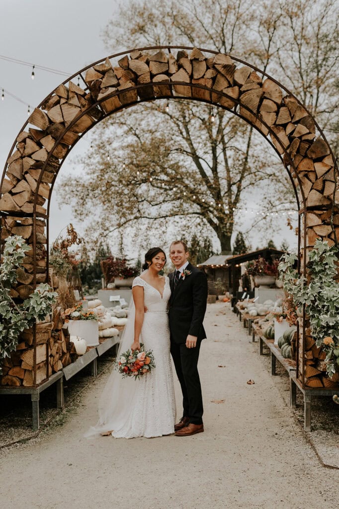 bride eand groom standing under arch of firewood at Terrain at Styer’s in Pennsylvania