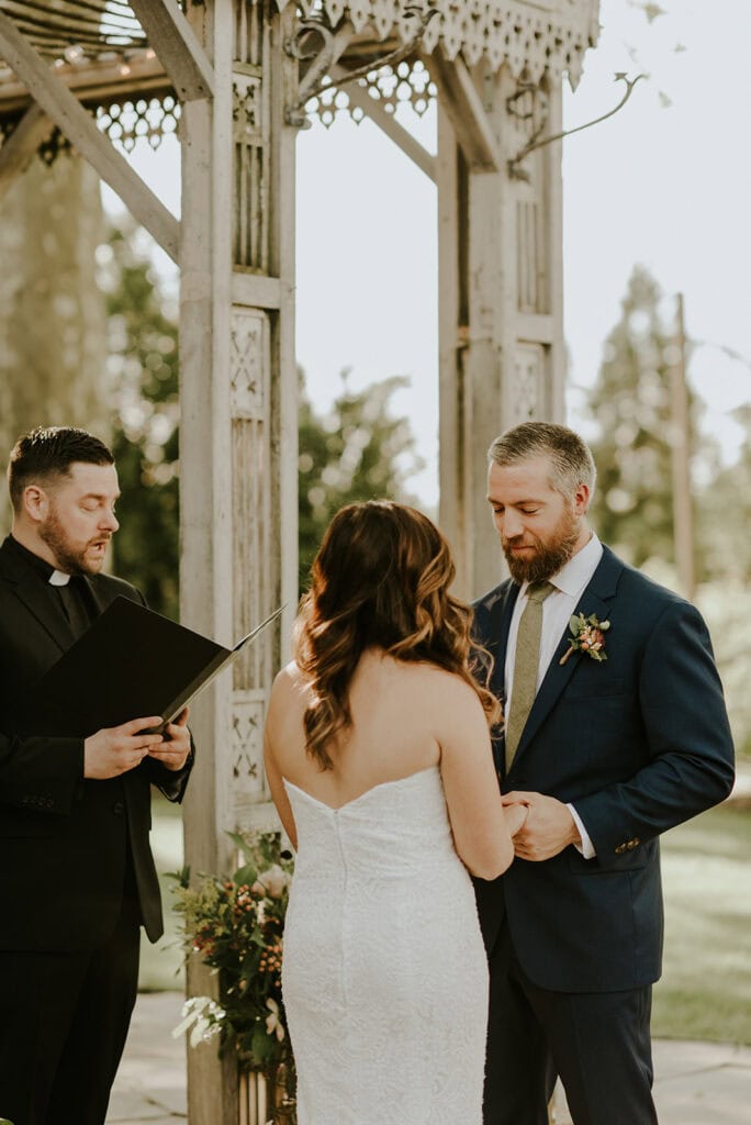 bride and groom exchanging vows in front of wedding officiant under the wooden wedding chapel at terrain wedding venue