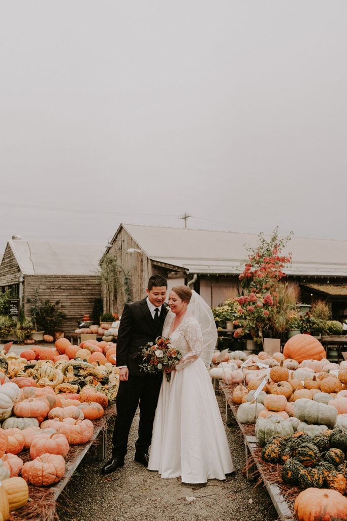 Bride and groom standing between rows of pumpkins at Terrain at Styer’s wedding venue