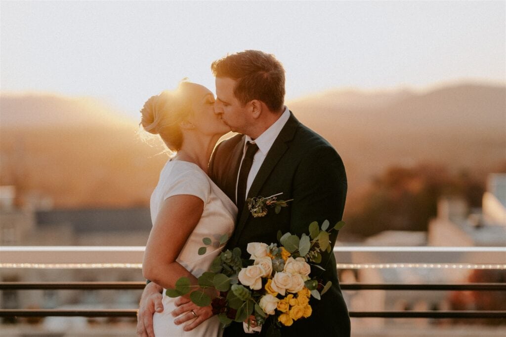 bride and groom kissing on hotel rooftop with mountains in background 