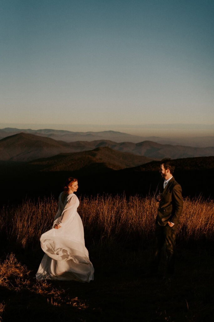 bride and groom in field with mountains in background 