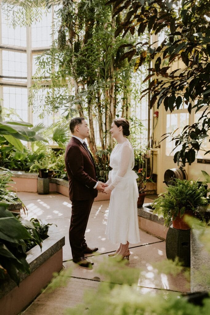 bride and groom walking around the rawlings conservatory during their baltimore elopement day surrounded by lush greenery and flowers