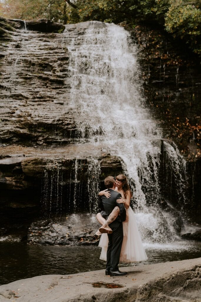 playful bride and groom in front of a waterfall at the swallow falls state park