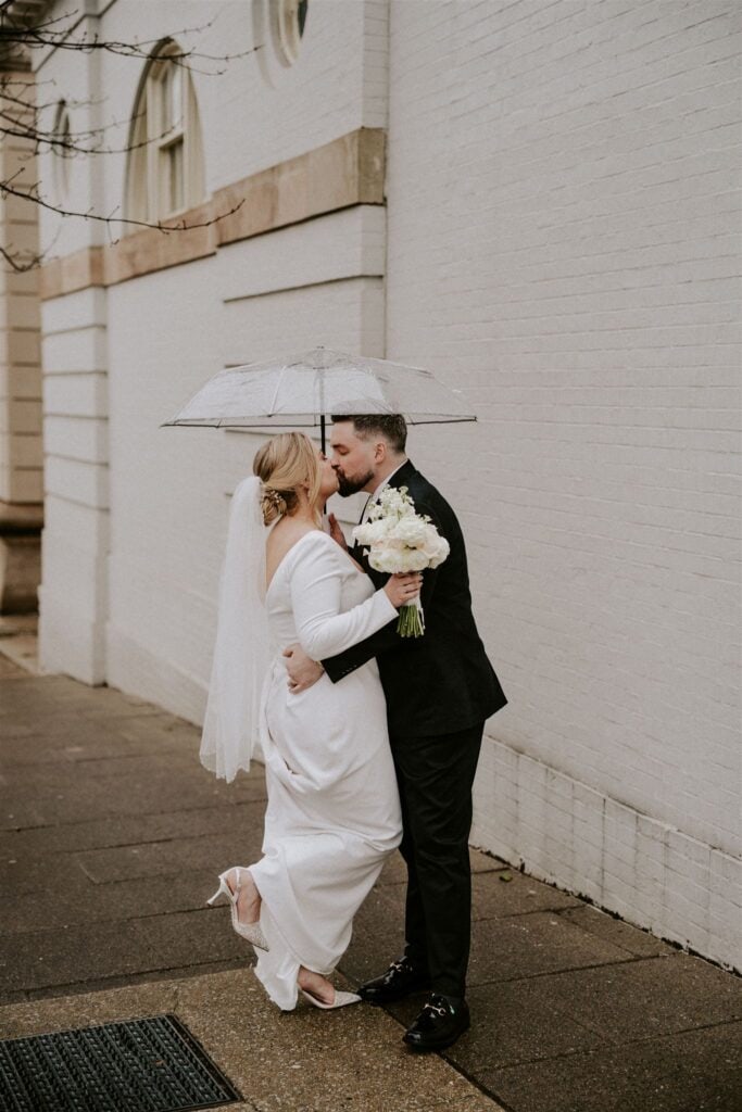 bride and groom walking in the city under a clear umbrella for their moody winter wedding in baltmore