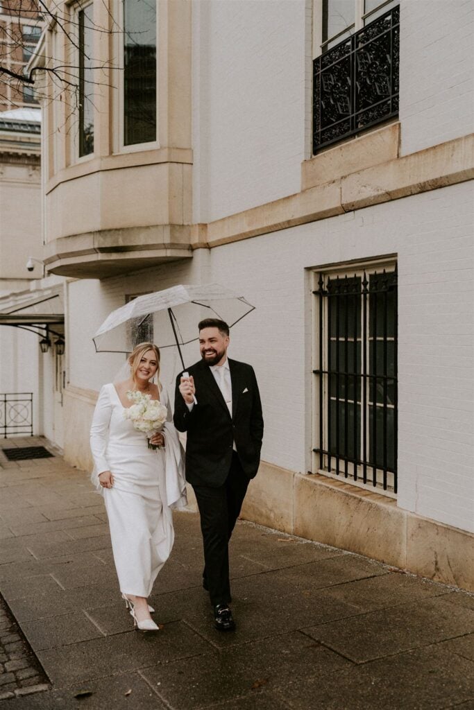 bride and groom walking in the city under a clear umbrella for their moody winter wedding in baltmore