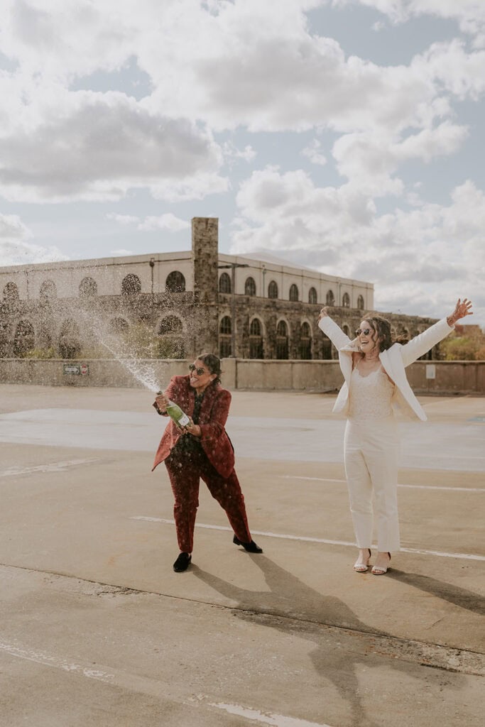 fun brides popping champagne on a rooftop