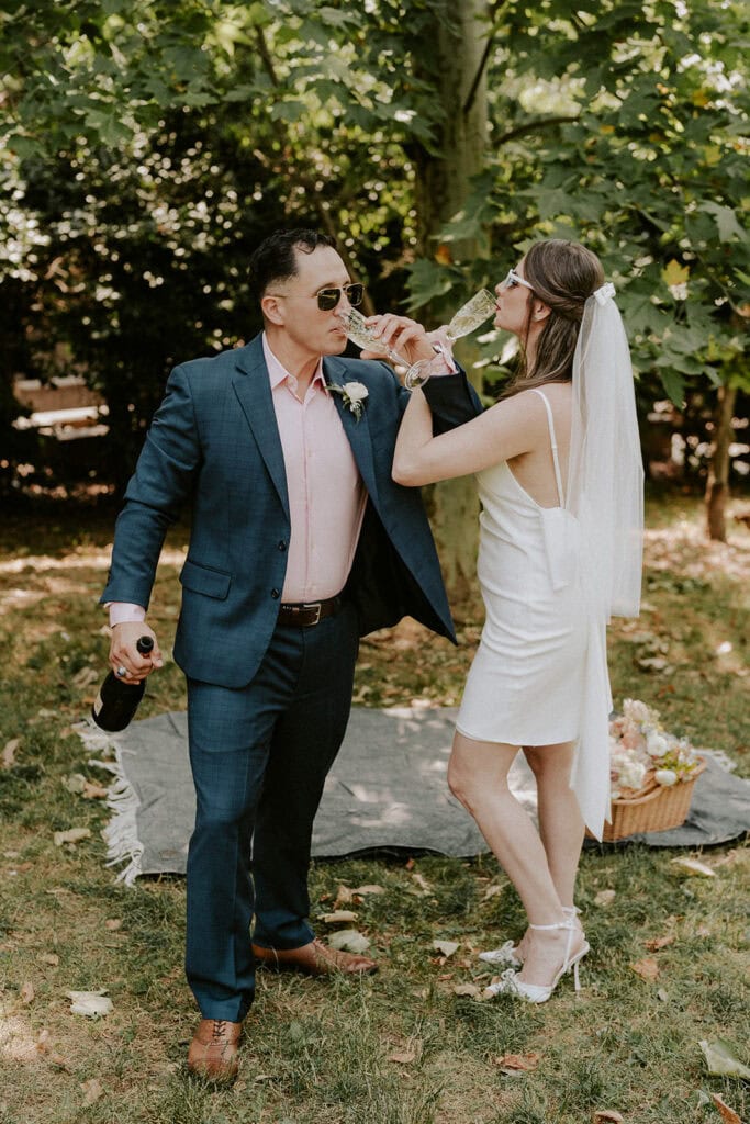 bride and groom popping champagne together during their elopement picnic in washington dc